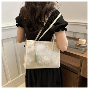 Détails de broderie florale et pompons sur un sac fourre-tout crème au style chinois