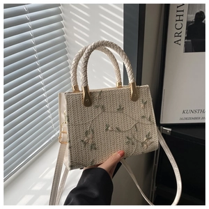 Detail of floral embroidery on a woven straw handbag with elegant top handles and strap