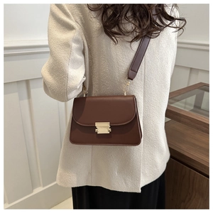 Detail of a vintage dark brown square bag with golden lock on a model shoulder