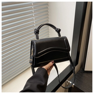 Close-up of black handbag with knotted handle detail and wavy edge flap design