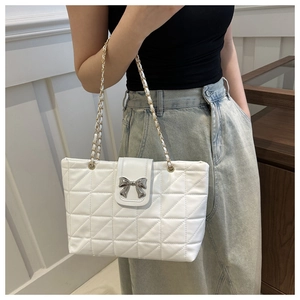 Detail of white quilted tote bag featuring a silver bow buckle and chain strap