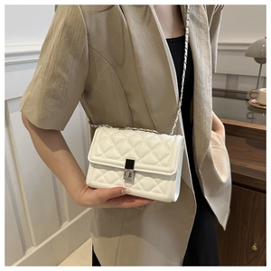 Detail of white quilted chain bag with silver lock on beige blazer outfit