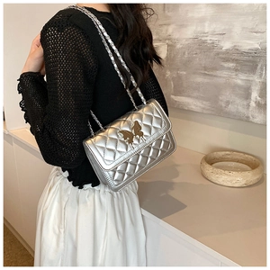 Sac bandoulière argenté matelassé avec fermoir papillon doré porté par un mannequin