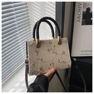 Close-up of floral embroidery on a straw handbag with black woven handles and strap