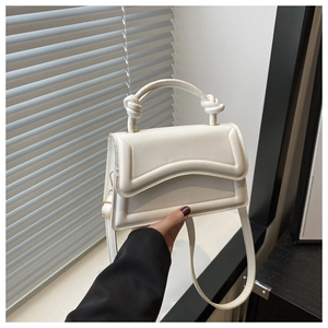 Detail of white geometric handbag with wavy stitching and knotted top handle design