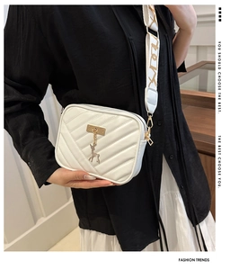 Detail of white chevron quilted crossbody bag with a golden deer charm and wide strap
