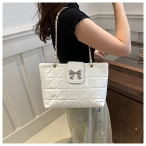 Detailed close-up of white quilted tote bag with silver bow and mixed chain strap
