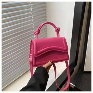 Detail of rose pink handbag featuring a knotted handle and wavy flap design with shoulder strap