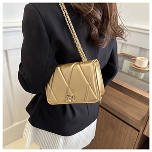 Detail of gold quilted crossbody bag with chain strap and metallic clasp on a model