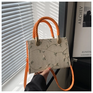Detail of floral embroidery on a woven straw bag with orange rope handles and leather strap