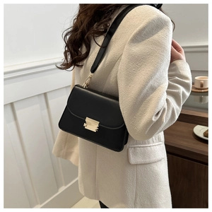 Detail of a black square shoulder bag with a gold rectangular metal buckle and wide strap