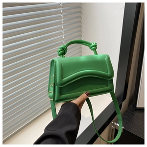 Close-up of bright green handbag featuring a twisted top handle and wave-edge flap detail