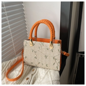 Detailed shot of beige woven straw handbag with green leaf embroidery and orange strap