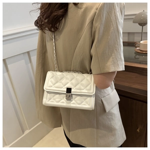 Detail of white quilted crossbody bag with silver chain worn over a beige blazer