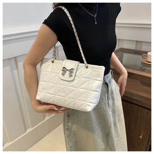 Detail of white quilted tote bag featuring a silver bow buckle and woven chain strap