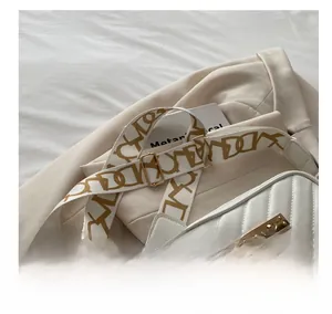 Close-up of white quilted crossbody bag with wide printed strap and deer charm