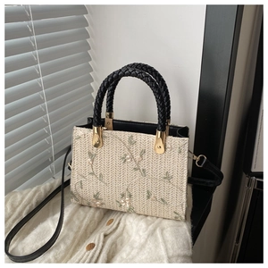 Detail of floral embroidery on beige woven handbag with black leather top handle