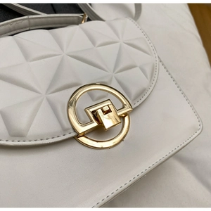 Detail of white crossbody bag featuring geometric triangle quilting and gold circular clasp