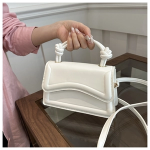 Close-up of white leather handbag featuring knot handle design and wavy flap detail