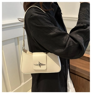 Detail view of cream leather underarm bag with silver star buckle worn by a model