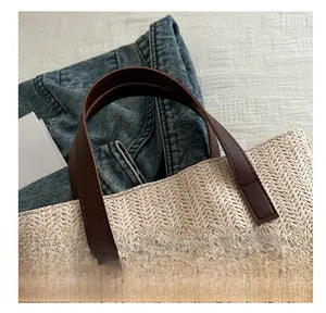 Close-up of woven straw handbag handle with dark brown leather and fine stitching details