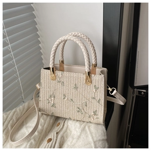 Detail view of a beige woven tote bag with delicate floral embroidery and gold metal hardware