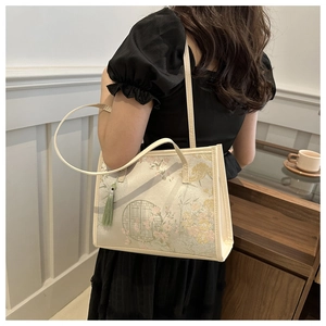 Détail du sac cabas beige à motifs floraux et pompon vert porté à l'épaule sur mannequin