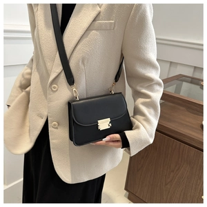 Close-up of a black leather crossbody bag featuring a polished gold rectangular clasp