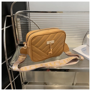 Detail of vintage yellow crossbody camera bag with V-quilted faux leather and golden deer charm