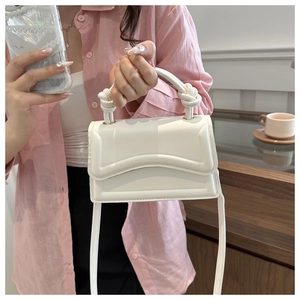 Detail of white mini handbag with wavy flap and knot handle worn on a pink shirt outfit