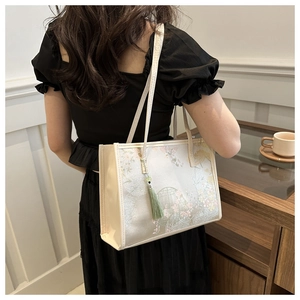 Détail du sac cabas floral avec pompon vert porté par un mannequin dans un café chic