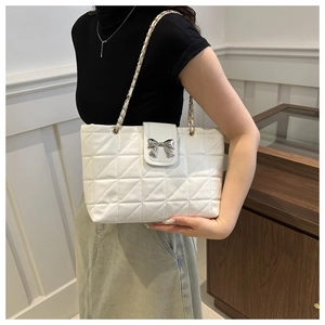 Close-up of a white quilted tote bag with a silver bow clasp and chain strap detail