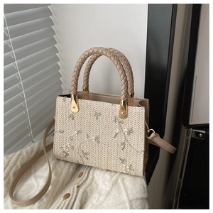 Detailed embroidery of light green and white flowers on a beige woven straw tote bag
