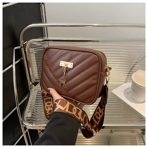 Detail of dark brown quilted crossbody bag with gold deer charm and wide pattern strap