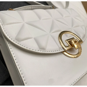Close-up of white crossbody bag with geometric 3D quilted texture and gold metal lock