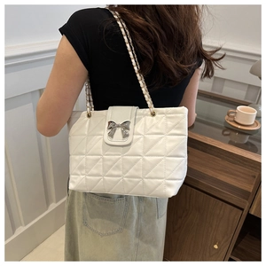 Detail of white quilted shoulder bag with silver bow accent and gold chain strap