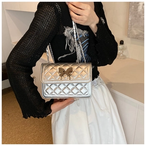 Détail du sac matelassé argenté avec boucle papillon dorée et bandoulière en chaîne