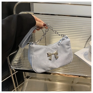Close-up of light blue shoulder bag featuring a silver metal bow and chunky chain detail