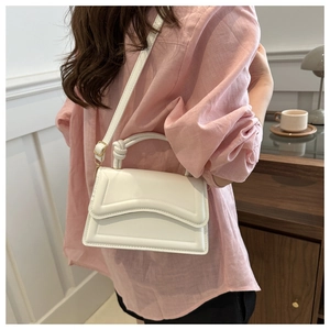 Detailed view of a white leather crossbody bag with knot handle worn by a model