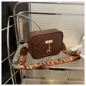Detailed view of brown quilted crossbody bag with gold elk pendant and wide strap