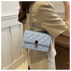 Detail of light blue quilted crossbody bag featuring silver chain strap and metal lock