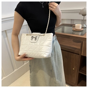 Detail view of quilted tote bag featuring silver bow clasp and woven chain strap on model