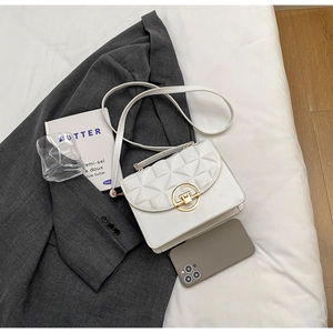 Close-up of white quilted crossbody bag with gold round clasp on a grey blazer