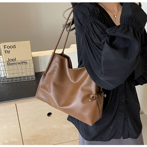 Brown soft faux leather tote bag with side knot detail shown on model in a modern room