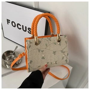 Close-up of vibrant orange woven tote bag featuring green leaf embroidery and braided handle
