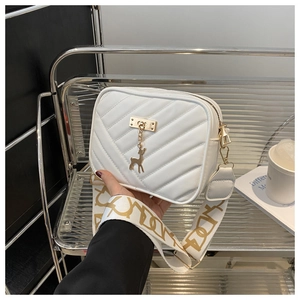 Close-up of white crossbody square bag with gold deer charm and patterned wide strap