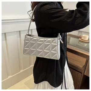 Detail of silver quilted shoulder bag with geometric pattern and thin strap shown on model