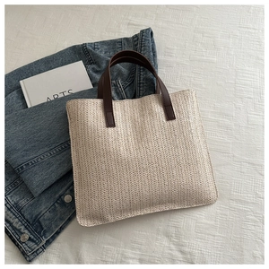 Close-up of a woven tote bag featuring brown leather handles and a textured cream finish