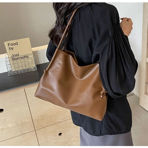 Close-up of caramel leather tote bag with decorative side knots worn by a model