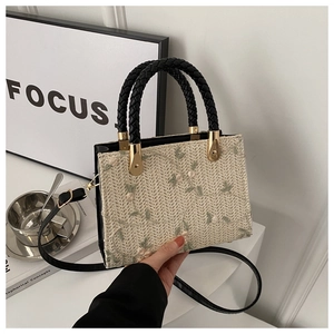 Detail of floral embroidery on beige straw handbag with black woven handles and strap